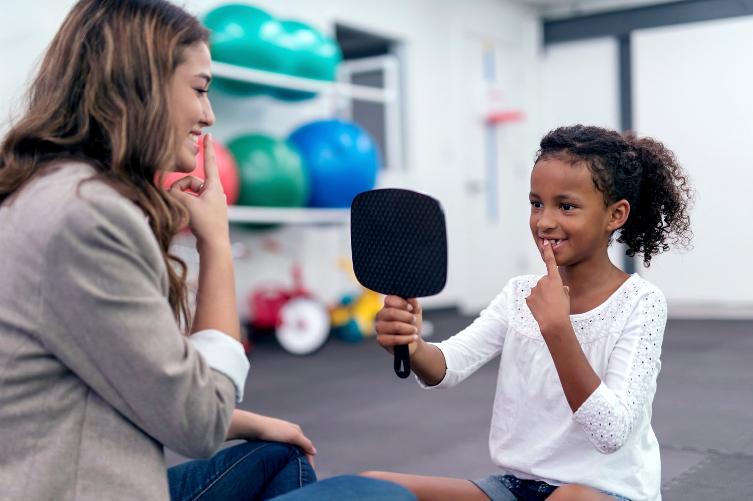 Cute African American girl using a mirror for speech therapy