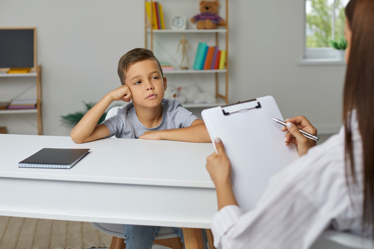 School Counselor, Psychologist or Teacher with Clipboard Talking to Child and Taking Notes